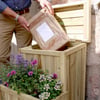 Bag of gardening soil being placed into a wooden garden planter box.