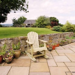 Adorable outdoor garden patio area with potted plants, a wooden chair, and a stone retaining wall in a lush, landscaped backyard. Perfect for relaxing in nature and outdoor gatherings.
