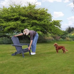 Bright outdoor garden scene featuring a woman with a dog on a lush green lawn, showcasing garden furniture and landscaping ideas from Empire Home and Garden for outdoor living.