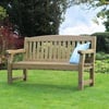 A wooden garden bench with a light blue cushion on lush green lawn surrounded by vibrant garden plants and trees.
