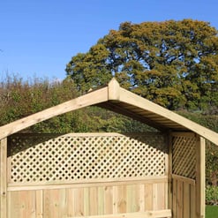 A wooden garden shed with lattice walls, set against lush greenery and a large tree with autumn foliage under a clear blue sky. Perfect for outdoor storage and garden organization.