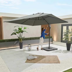A woman adjusting a large outdoor patio umbrella on a modern home patio with potted plants, lanterns, and outdoor decor, showcasing backyard furniture and garden accessories.