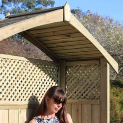 A woman relaxing outdoors in a garden reading a book under a custom-built wooden lattice and privacy fence by Empire Home and Garden.