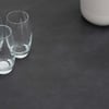 Crystal-clear drinking glasses arranged on a sleek dark surface, with a modern white vase partially visible in the background, showcasing stylish home decor and tabletop essentials.