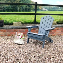 Adirondack chair on a gravel patio with floral decor and garden planters in the background.