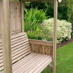 Wooden garden bench under a backyard pergola with lush garden flowers and greenery in the background, perfect for outdoor relaxation and garden decor.
