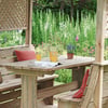 Rustic outdoor wooden dining set with cushions, surrounded by lush garden with vibrant flowers and greenery, ideal for garden furniture, backyard patio, outdoor dining, and relaxation.