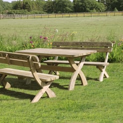 Rustic wooden outdoor picnic table and benches on lush green lawn with colorful flowers and rural landscape, ideal for garden gatherings and outdoor dining.