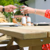 Enjoying outdoor dining on a wooden patio table with friends, featuring wine glasses, a delicious meal, and sunny garden surroundings. Perfect for backyard gatherings and summer entertainment.