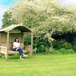 Natural wooden garden arbor with sitting area in lush landscape.