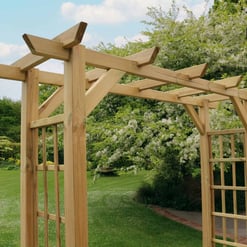 Natural wooden garden arbor in a lush outdoor setting with blossoming trees. Perfect for enhancing your yard with durable, stylish landscape architecture and outdoor garden features.