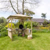 Colorful garden outdoor gazebo with a grill and gardening supplies in a lush backyard garden.