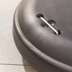 Shallow depth of field close-up image of a black cast iron skillet handle with a metal rivet on a light-colored countertop, showcasing durable kitchen cookware for home and garden use.