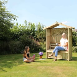 Cozy wooden garden gazebo with bench seating nestled in a lush backyard with vibrant greenery and colorful flowers, ideal for outdoor relaxation and leisure activities.