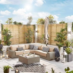 Stylish outdoor patio with beige sectional sofa, decorative pillows, modern lanterns, lush greenery, and privacy wooden fencing, perfect for outdoor entertaining and relaxation.