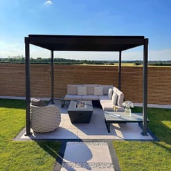 Modern outdoor patio with a black pergola, comfortable sectional sofa, fire pit, and surrounding lush green lawn, perfect for entertaining in a stylish backyard setting.