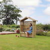 Elegant wooden garden gazebo with a woman sitting on built-in bench, surrounded by lush greenery and colorful flowers, perfect for outdoor relaxation and garden enhancement.
