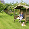 Relaxing garden sitting area with a woman enjoying the outdoor space, surrounded by vibrant flowers, lush greenery, and a wooden garden shelter for comfortable garden leisure and outdoor living.