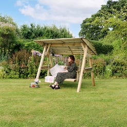 Relaxing garden swing with a woman enjoying the outdoors, surrounded by lush greenery and colorful flowers, ideal for outdoor furniture and garden decor.