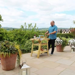 Enjoying outdoor cooking on a sunny garden patio surrounded by lush landscaping and potted plants, perfect for entertaining and relaxing in a beautiful backyard setting.