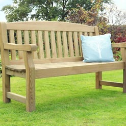 Natural wood garden bench with a light blue decorative pillow, surrounded by lush greenery and colorful shrubs, perfect for outdoor relaxation and garden decor.