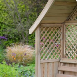 Natural wood garden shed with lattice details and a sloped roof in a lush green garden setting.