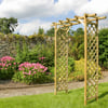 Wooden garden arbor with lattice panels in a lush, landscaped backyard with blooming pink flowers and stone wall.