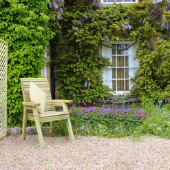 Beautiful garden seating area with wooden chair, vibrant flowers, lush greenery, and ivy-covered brick wall, perfect for outdoor home garden oasis.