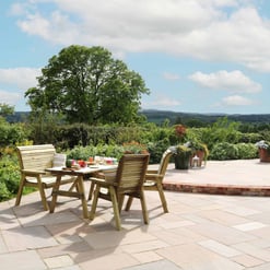 Sunny outdoor patio with wooden dining table and chairs, surrounded by lush greenery and vibrant potted flowers, perfect for garden entertaining and relaxing in a beautiful landscape.