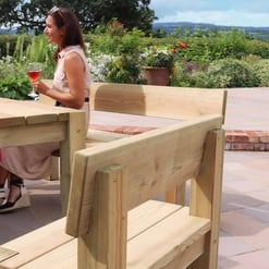 Natural wood outdoor dining table and benches on a patio, surrounded by potted plants and garden scenery, perfect for outdoor entertainment and relaxation.