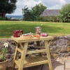 Rustic wooden outdoor table set on stone patio with garden and lush lawn in the background, ideal for garden dining and outdoor entertaining, featuring a wine bottle, glasses, and picnic accessories.