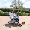 Relaxing woman sitting on a stylish Adirondack chair outdoors on a beautiful patio surrounded by lush garden with blooming flowers, ideal for outdoor living and garden furniture at Empire Home and Garden.