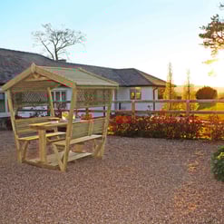 Garden patio with wooden outdoor furniture during sunset, featuring lush landscaping and a scenic backyard view, ideal for outdoor living and garden design.