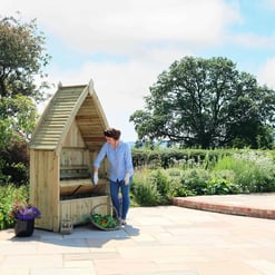 Handcrafted outdoor wooden compost bin on patio, with woman gardening and composting vegetable scraps in a beautiful garden setting, sunlight, and scenic landscape, ideal for eco-friendly gardening.