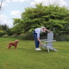 Ad 1: Woman placing Adirondack chair on lush green lawn with dog nearby in a spacious backyard.