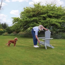 Ad 1: Woman placing Adirondack chair on lush green lawn with dog nearby in a spacious backyard.