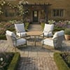 Elegant outdoor seating area with comfortable white cushioned chairs around a wooden table, set on a charming brick patio amidst lush garden flowers and a rustic stone house backdrop.