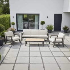 Sleek modern outdoor patio furniture set with white cushions and a matching coffee table, surrounded by potted plants, in a contemporary backyard space.