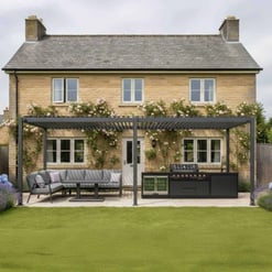 Elegant backyard outdoor kitchen with built-in grill, outdoor seating, and pergola, perfect for entertaining in a landscaped garden behind a classic stone house.
