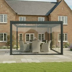 Modern glass outdoor patio enclosure with black frame, providing a stylish and weather-resistant space for outdoor dining or relaxation, set against a traditional brick house.