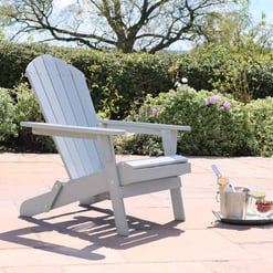Adirondack chair on a patio with a tray holding a bottle, wine glass, and strawberries in front of lush garden hedges with blooming flowers, ideal for outdoor home and garden relaxation.