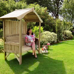 Relaxing garden seating area with wooden outdoor bench under a small wooden shelter in lush, landscaped backyard. Perfect for gardening, outdoor relaxation, and enjoying nature.