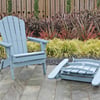 Colorful Adirondack chairs and footstools set on a stone patio in a landscaped garden with ornamental grasses and a wooden fence.