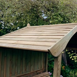 Wooden garden playhouse with a sloped roof, in a lush outdoor setting with trees and flowering plants. Ideal for children's outdoor play, garden decor, or backyard landscaping.