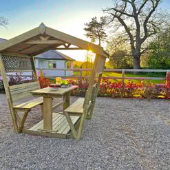 Rustic wooden outdoor gazebo with seating, providing a relaxing garden space at sunset, perfect for outdoor dining and leisure activities, surrounded by lush landscaping.