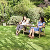 Relaxing outdoor garden seating with two women enjoying wine and conversation on a sunny day. Beautiful lush greenery and vibrant plants create a peaceful ambiance for outdoor gatherings.