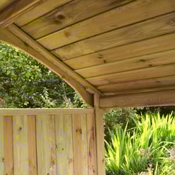 Cedar garden shed with wood siding and a curved roof, surrounded by lush green foliage and flowering plants. Perfect for outdoor storage or garden workspace.