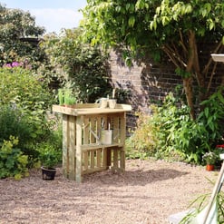 Rustic wooden garden potting station with watering can, surrounded by lush greenery in a backyard garden. Perfect for outdoor gardening and plant care.
