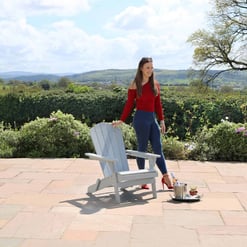 Elegant woman enjoying outdoor patio with Adirondack chair, wine and beautiful garden scenery at Empire Home and Garden.