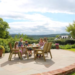 Outdoor wooden dining set on a patio with garden and scenic landscape, ideal for backyard entertaining and outdoor gatherings. Perfect for garden furniture and patio design enthusiasts.